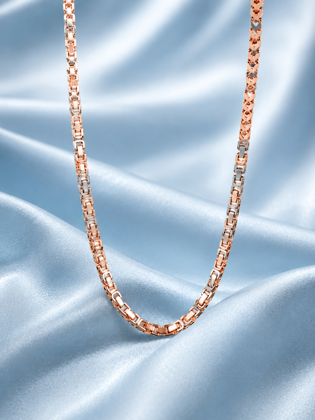 A close-up of a rose gold chain necklace draped over a light blue satin fabric background.