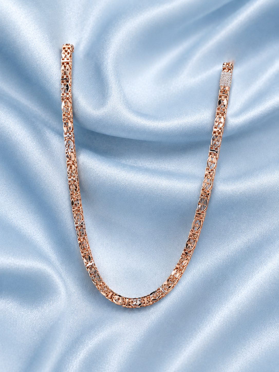 A rose gold tennis-style link chain necklace arranged in a U-shape on a light blue satin fabric background.