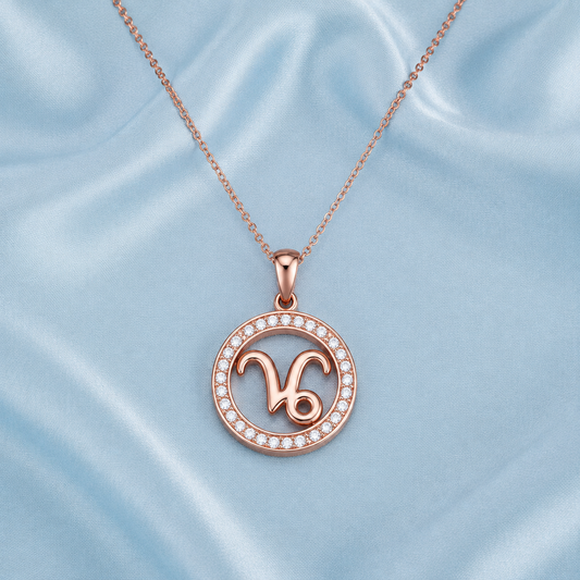 A rose gold necklace with a circular pendant featuring the Virgo zodiac symbol, set against a light blue satin fabric background.