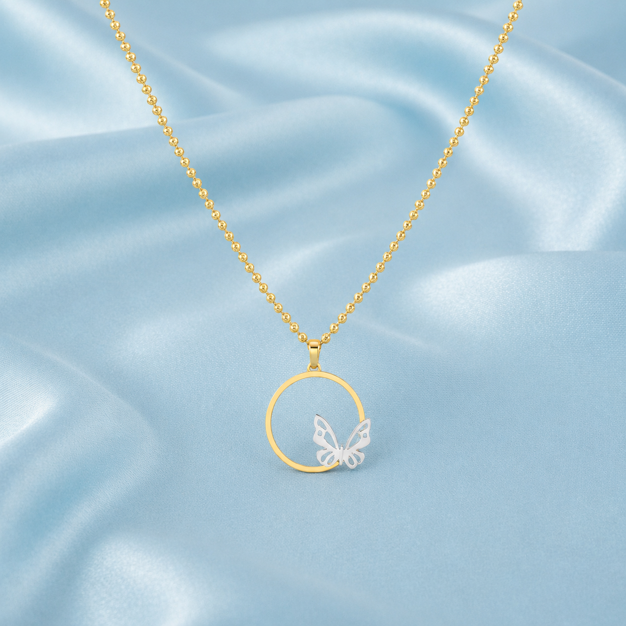 A gold chain necklace with a circular pendant featuring a small white butterfly, displayed on a light blue satin fabric background.