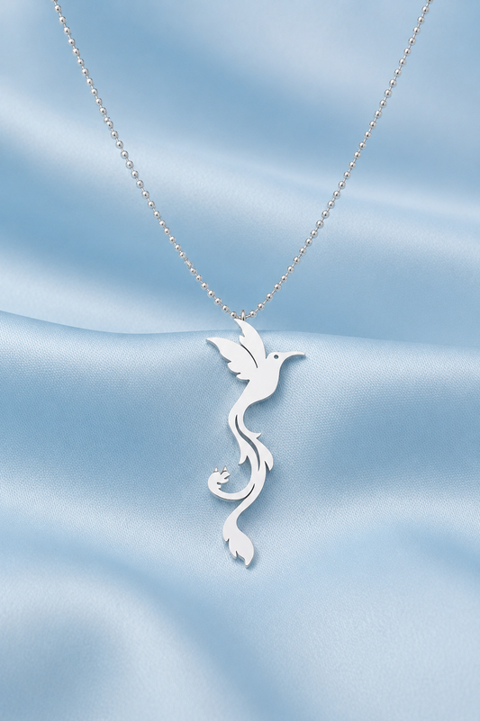A silver necklace with a stylized bird pendant on a delicate chain, displayed against a soft, light blue satin fabric background.