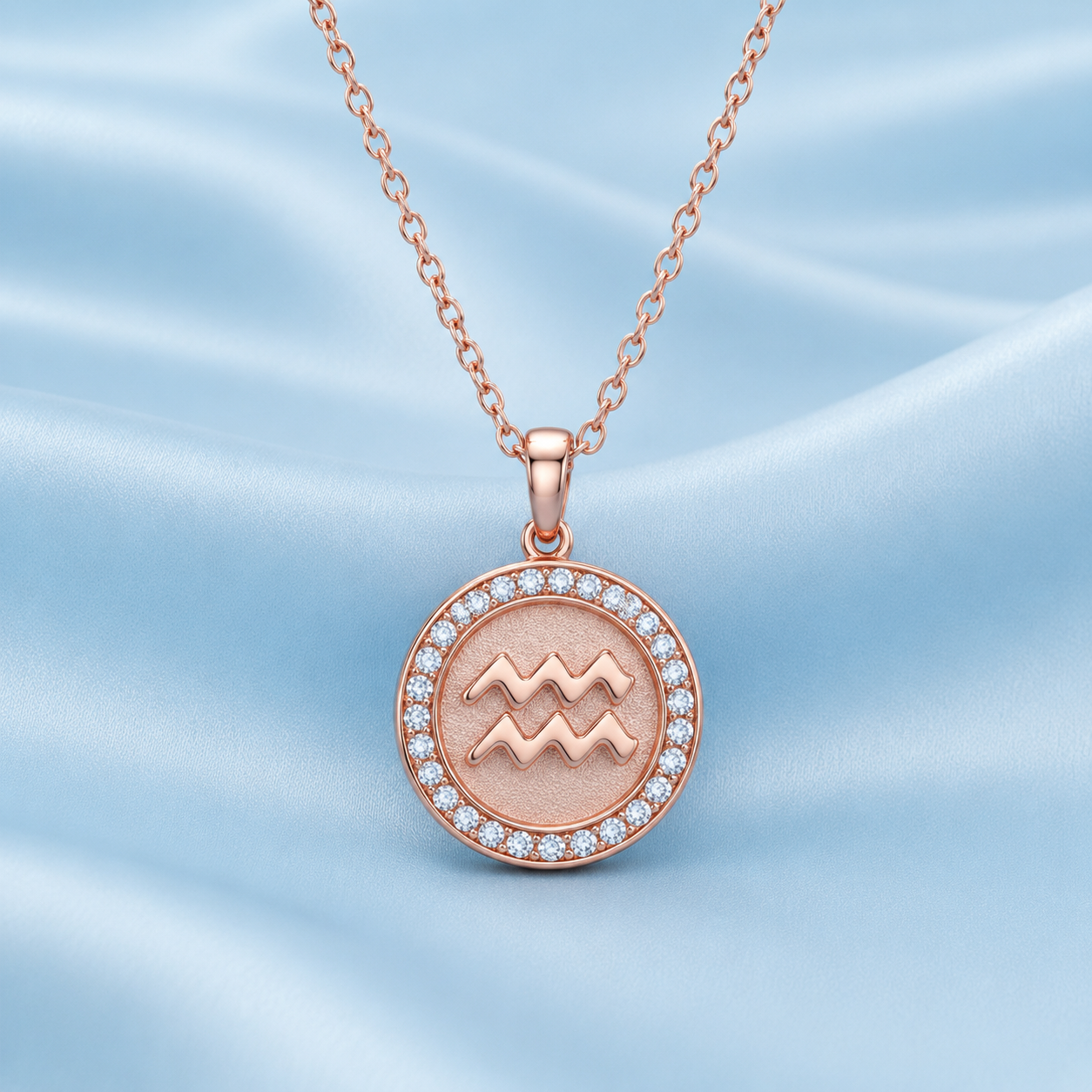 A rose gold pendant necklace featuring the Libra zodiac sign, set in a circular bezel with small clear stones, displayed on a light blue satin fabric background.