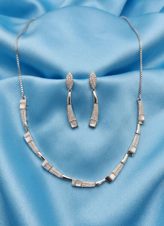 Silver-tone jewelry set featuring a necklace and matching drop earrings, displayed on a draped light blue satin fabric background.