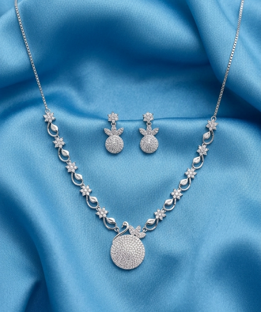 Silver jewelry set featuring a necklace and matching earrings with floral and teardrop motifs, displayed on a draped light blue satin fabric.