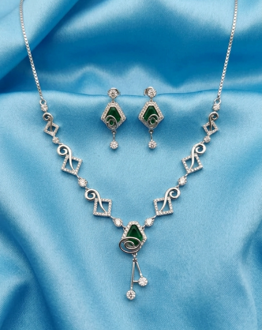 Silver-tone jewelry set featuring a necklace and matching earrings with green inlay and clear rhinestone accents, displayed on a draped light blue satin fabric background.