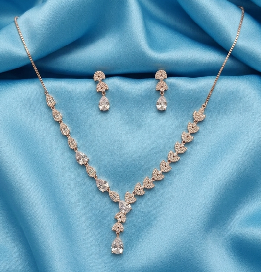 Rose gold jewelry set featuring a necklace and matching drop earrings with clear teardrop and oval stones, displayed on a draped light blue satin fabric background.