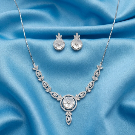 Silver-tone jewelry set featuring a necklace and matching earrings, both adorned with clear crystals, displayed on a draped light blue satin fabric background.