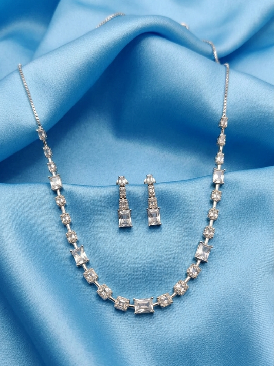 Silver-tone jewelry set featuring a necklace and matching drop earrings with clear rectangular gemstones, displayed on draped light blue satin fabric.