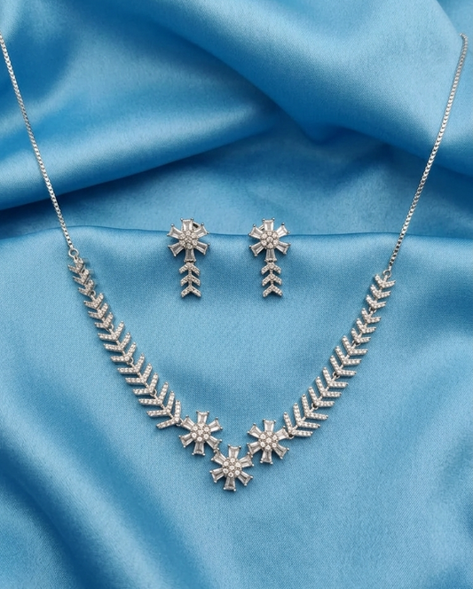 Silver-toned jewelry set featuring a necklace and matching earrings with snowflake and chevron motifs, displayed on a draped light blue satin fabric background.