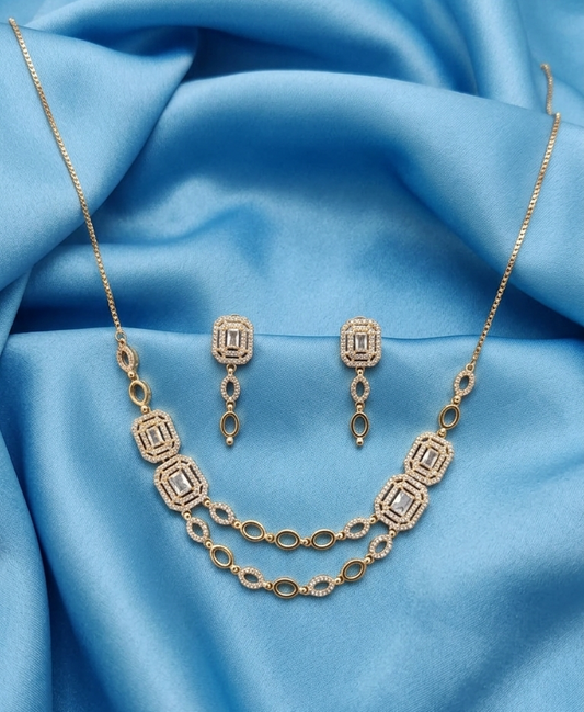 Gold jewelry set featuring a necklace and matching drop earrings, displayed on draped light blue satin fabric.
