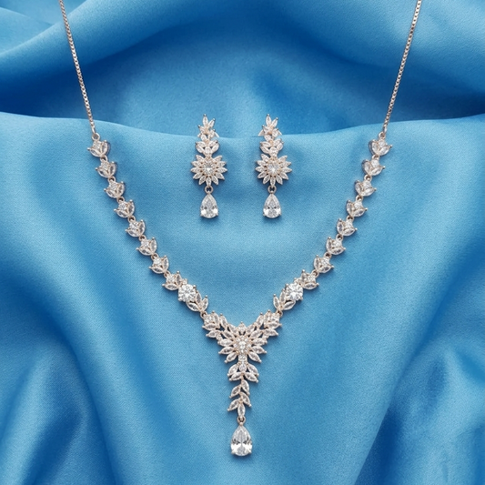 Silver-tone floral jewelry set with a V-neck necklace and matching drop earrings, displayed on a draped light blue satin fabric background.